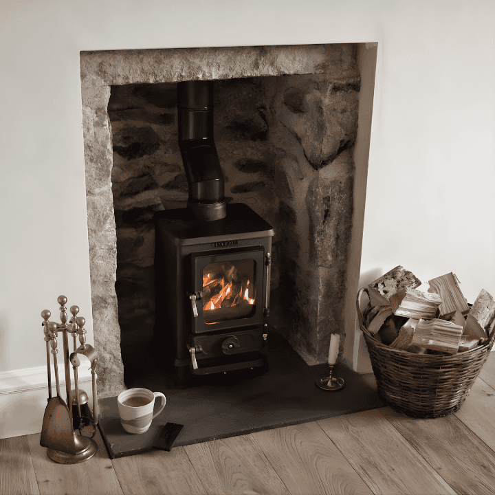 Modern wood stove in a stone fireplace with cozy decor and fire burning.